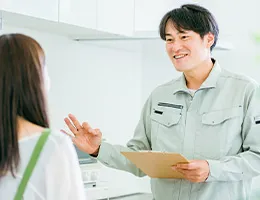 作業服の男性がエプロンを付けた女性にキッチンで設備の説明をしている