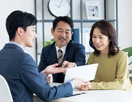 中年の夫婦がスーツの男性スタッフから資料を基に説明を受けている