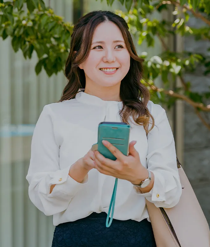 スマートフォンを操作しながら周囲を見る白いブラウスを着用した女性